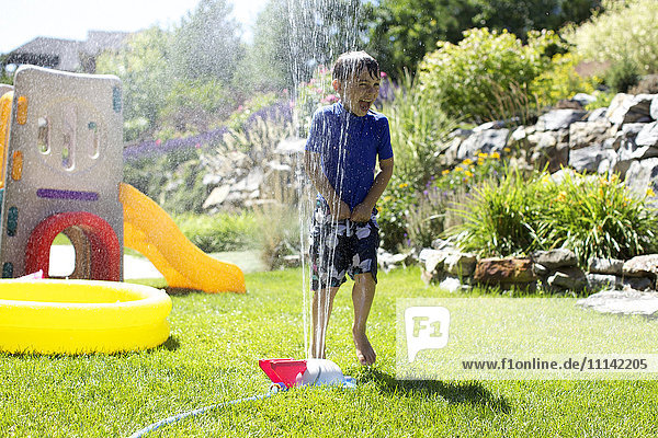 Caucasian boy playing in backyard sprinkler