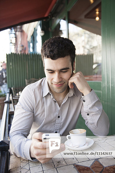 Hispanic man using cell phone at sidewalk cafe