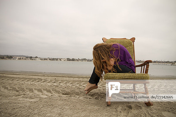 Frau in Sessel am Strand sitzend
