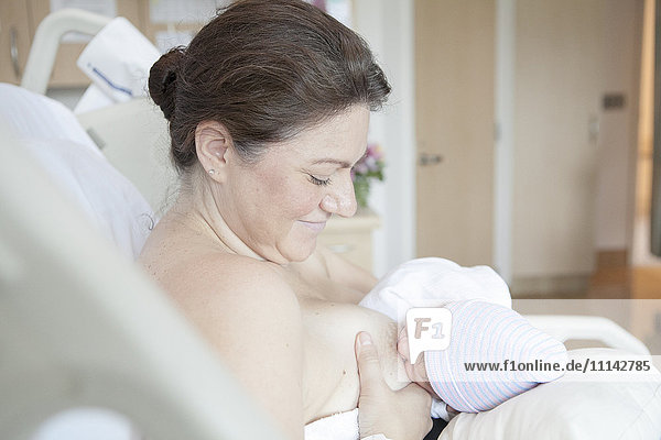 Caucasian mother nursing newborn daughter in hospital bed