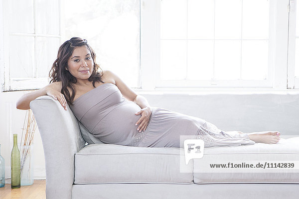 Schwangere hispanische Frau mit Bauch auf dem Sofa