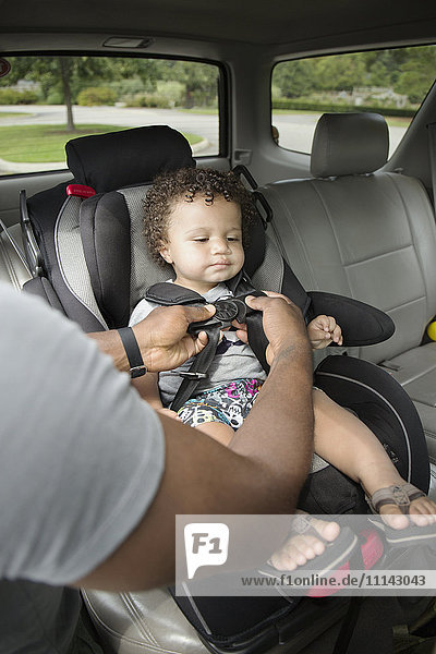 Vater schnallt sein Kleinkind im Autositz an