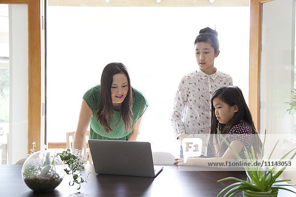 Mutter und Töchter benutzen Laptop im Esszimmer