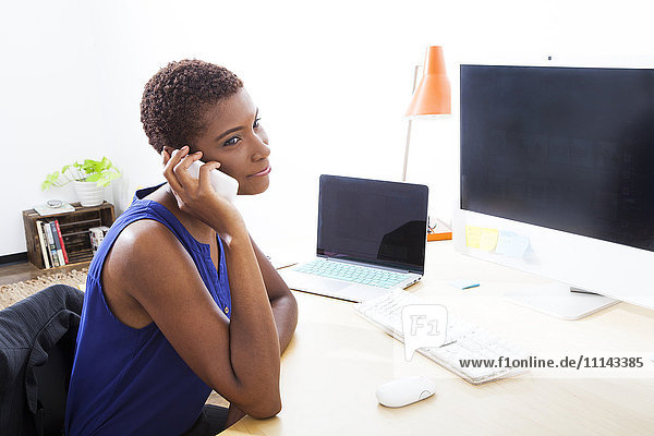 Schwarze Geschäftsfrau  die am Schreibtisch mit ihrem Handy telefoniert