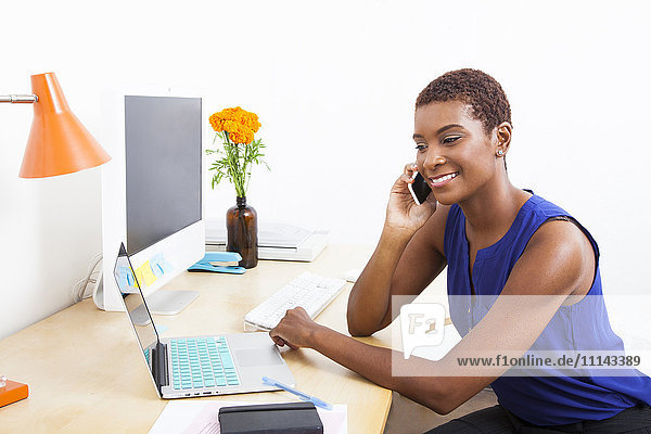 Schwarze Geschäftsfrau  die am Schreibtisch mit ihrem Handy telefoniert