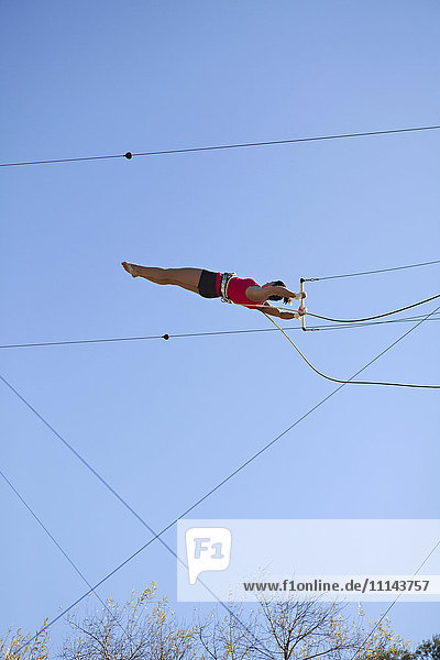 Acrobat hanging from trapeze under blue sky