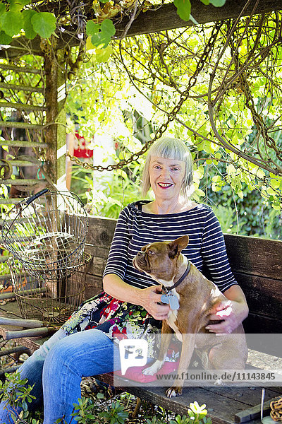 Ältere kaukasische Frau streichelt Hund im Garten