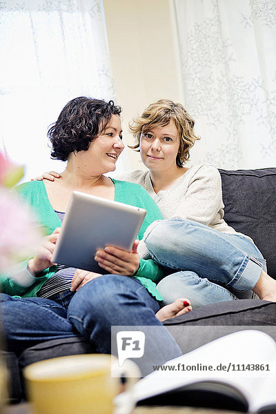 Lesbisches Paar benutzt digitales Tablet auf Sofa im Wohnzimmer