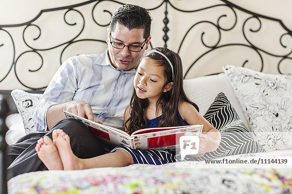Father reading to daughter on bed