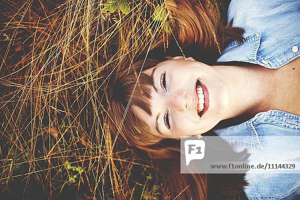 Nahaufnahme einer lächelnden Frau,  die im hohen Gras liegt