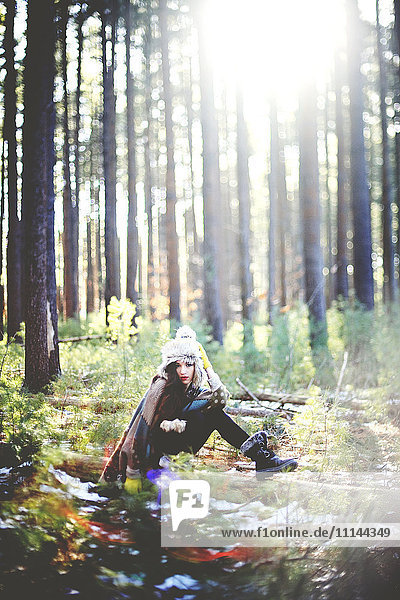 Frau sitzt auf einem Baumstamm im Wald