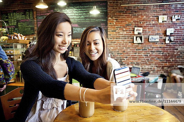 Women taking selfie with cell phone at cafe table