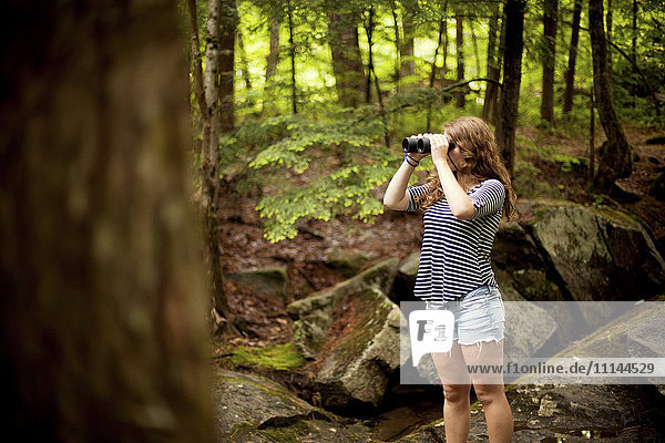Girl looking through binoculars in forest