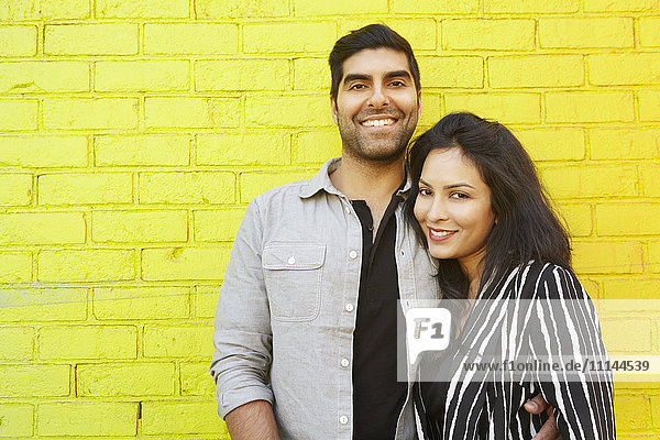 Indisches Paar  das sich vor einer gelben Backsteinmauer umarmt