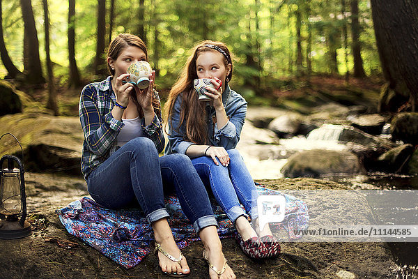 Mädchen trinken Kaffee auf einem Waldfelsen