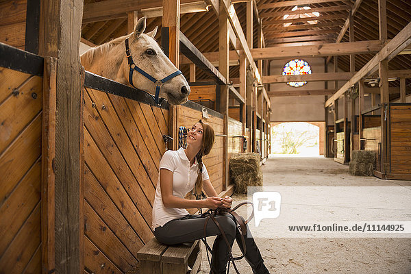 Kaukasisches Mädchen sitzt mit Pferd im Stall