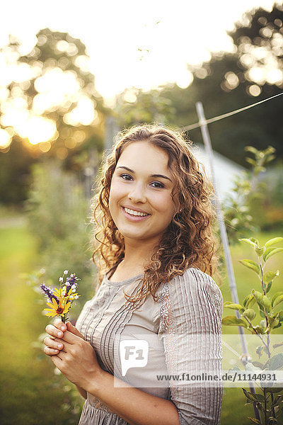 Lächelnde Frau hält Blume im Garten