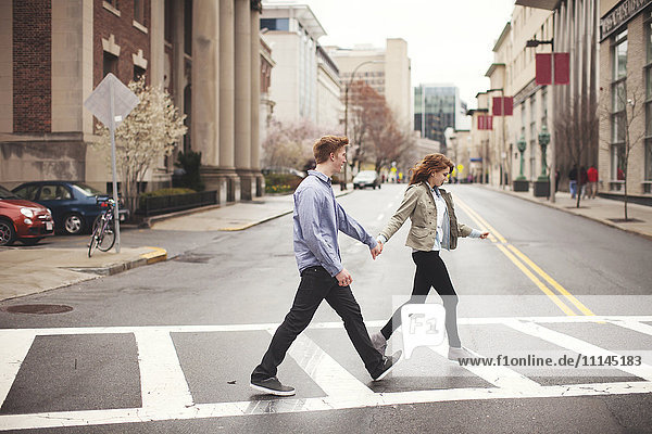 Caucasian couple holding hands crossing city intersection