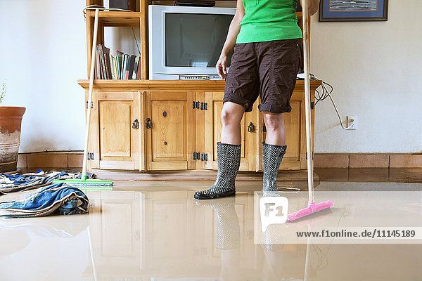 Hispanische Frau kehrt Wasser aus überflutetem Haus