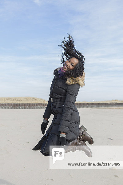 Frau im Mantel springt vor Freude am Strand