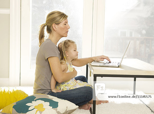 Mutter und Tochter benutzen einen Laptop im Wohnzimmer