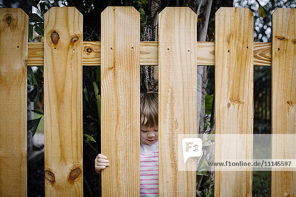 Gemischtrassiges Mädchen schaut durch den Holzzaun im Hinterhof