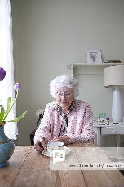 Ältere Frau trinkt Tee am Tisch