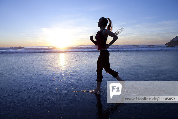 Silhouette einer Frau  die bei Sonnenaufgang am Strand läuft