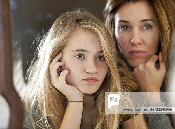 Serious mother and daughter examining themselves in mirror
