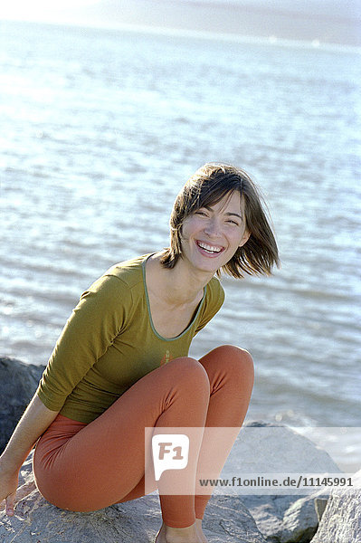 Gemischtrassige Frau lächelnd auf Felsen am Strand