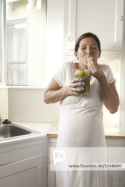 Pregnant woman eating pickles in kitchen