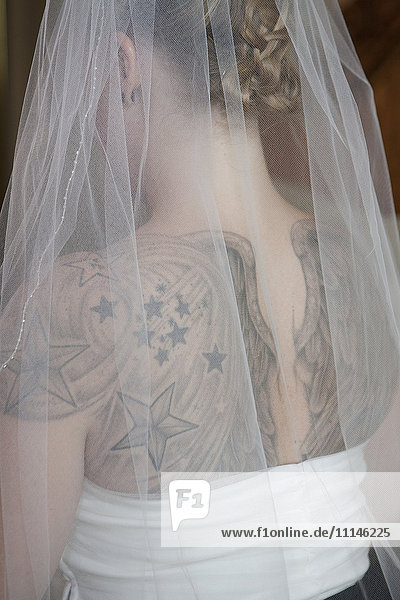 Rückansicht einer kaukasischen Braut mit Schleier und Tattoos auf dem Rücken