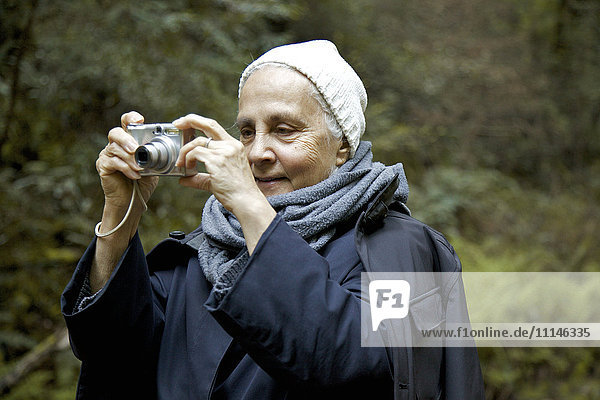 Nahaufnahme einer älteren Frau beim Fotografieren im Wald