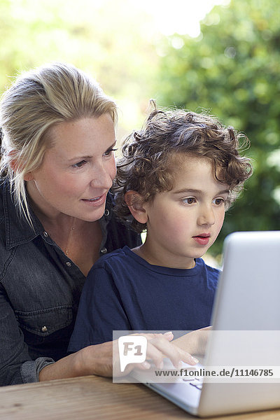 Mutter und Sohn benutzen Laptop am Tisch