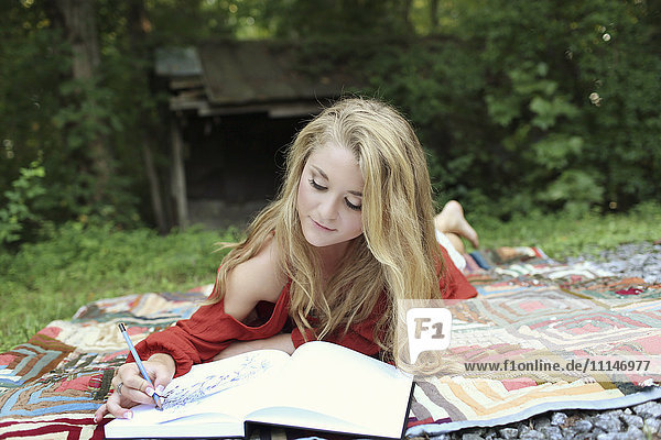 Teenage girl drawing in notebook on blanket
