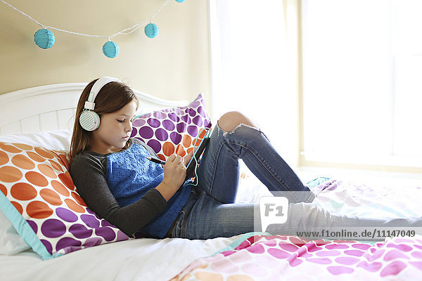 Girl listening to headphones with digital tablet on bed