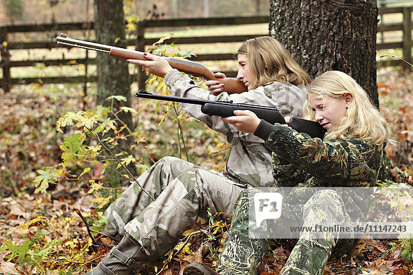 Mutter und Tochter in Camouflage zielen im Wald auf Gewehre