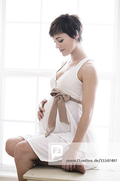 Schwangere Frau hält ihren Bauch am Fenster