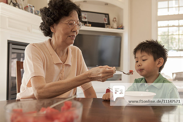 Asian grandmother feeding grandson at table