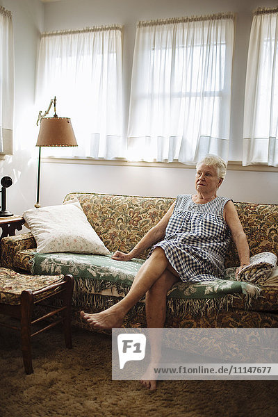 Ältere Frau sitzt auf dem Sofa im Wohnzimmer
