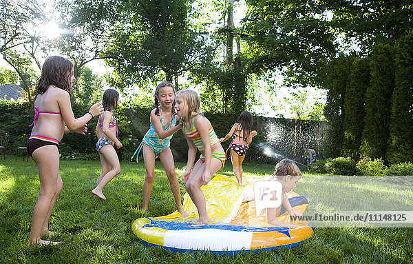 Children playing on water slide in backyard