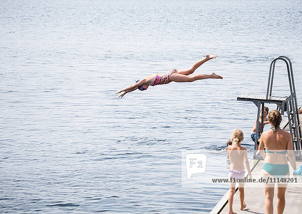 Kaukasisches Mädchen springt vom Sprungbrett in den See