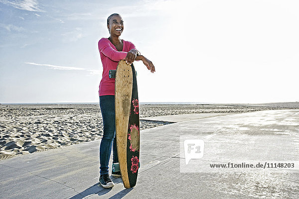 Ältere schwarze Frau hält Skateboard am Strand