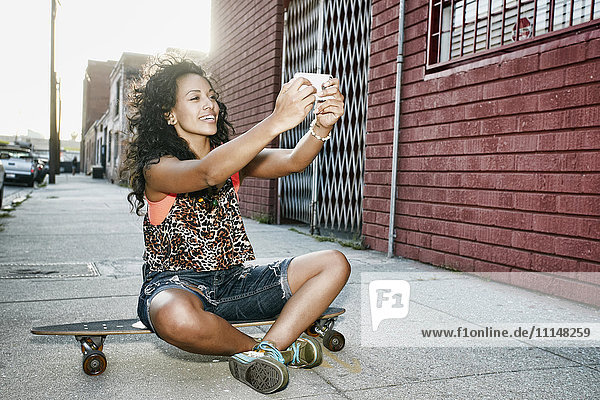 Hispanische Frau macht Handy-Foto auf Skateboard auf der Straße