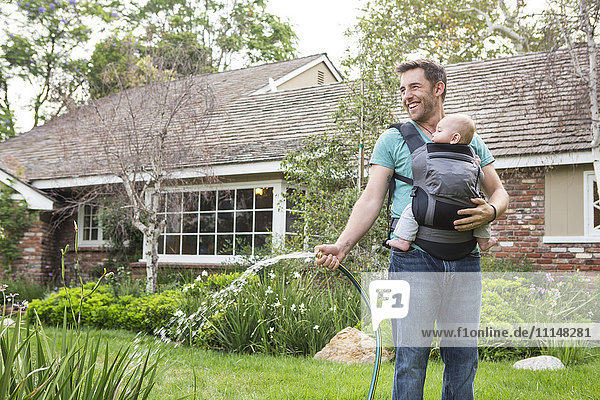 Caucasian father holding baby and watering plants