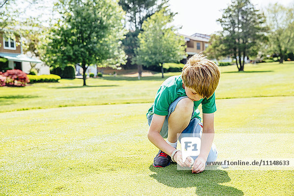 Caucasian boy setting up golf ball on course