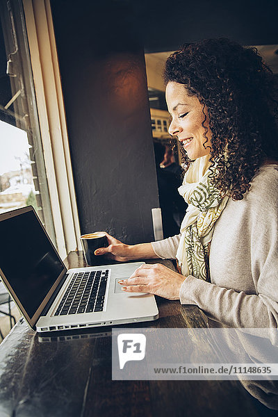 Frau benutzt Laptop und trinkt Kaffee in einem Cafe