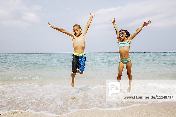 Gemischtrassige Kinder springen vor Freude am Strand