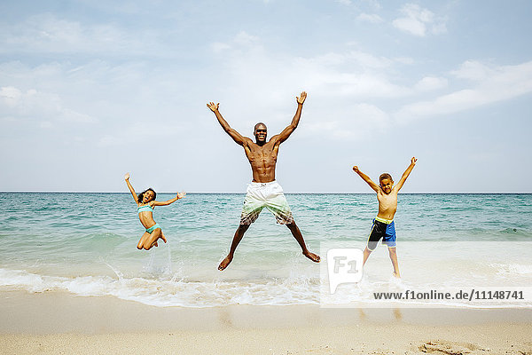 Vater und Kinder springen vor Freude am Strand