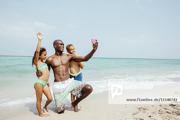 Vater und Kinder machen ein Selfie am Strand